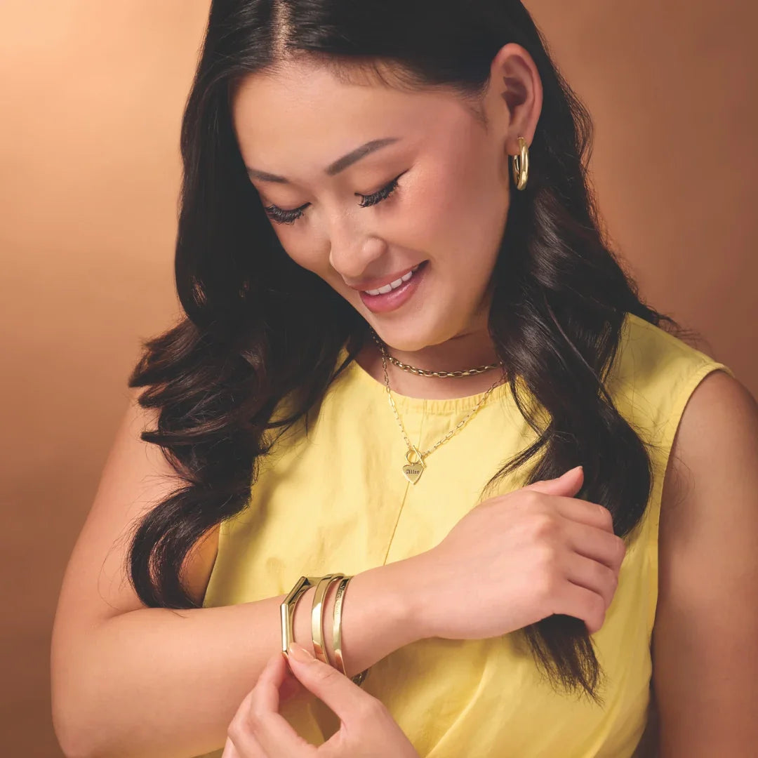Woman wearing stacked gold bracelets, a gold necklace and gold hoop earrings