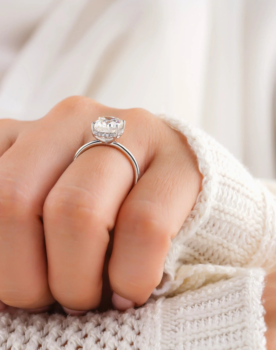 Hand in a cream knit sweater wearing a halo diamond engagement ring in white gold