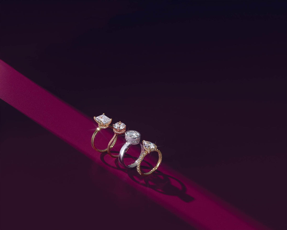 Four elegant diamond engagement rings in gold and platinum, featuring radiant cuts and halo settings on a deep red velvet.