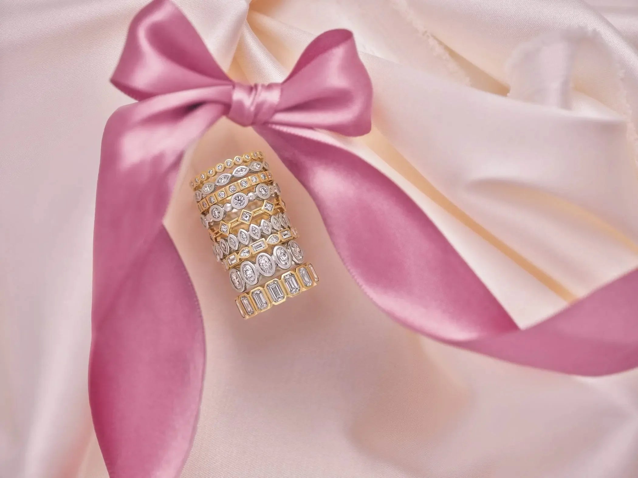 Stacked gold diamond rings on soft satin with a pink ribbon, fine jewelry display