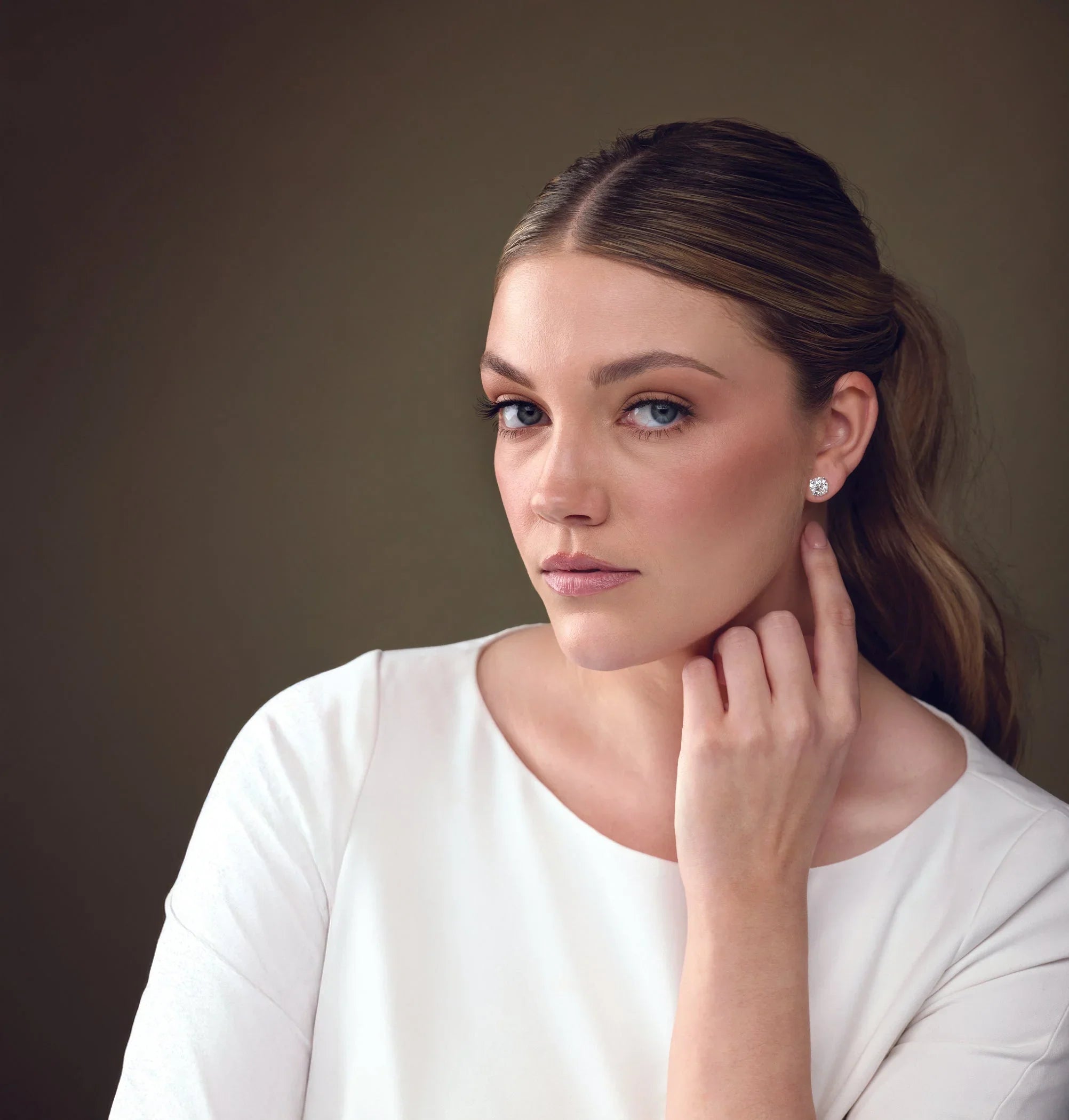 Woman wearing white top displaying round diamond stud earrings