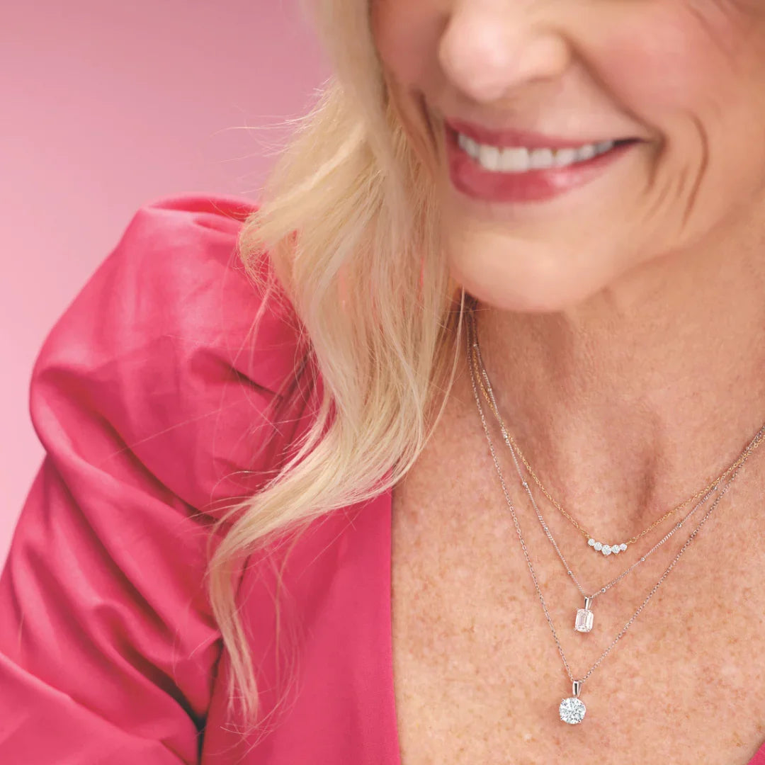 Woman wearing layered diamond pendant necklaces on gold and silver chains, pink top