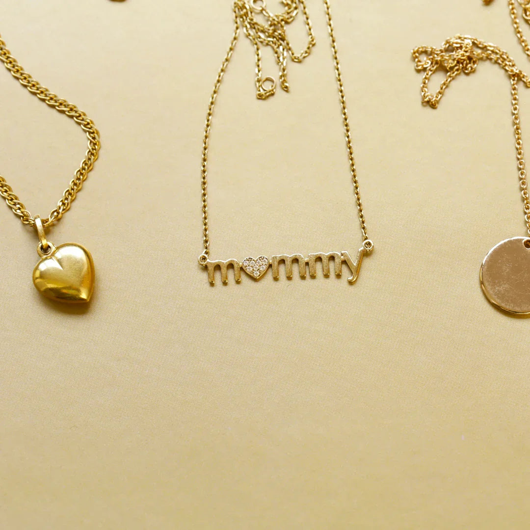 Gold pendant necklaces on beige background, featuring heart and mommy designs with diamonds
