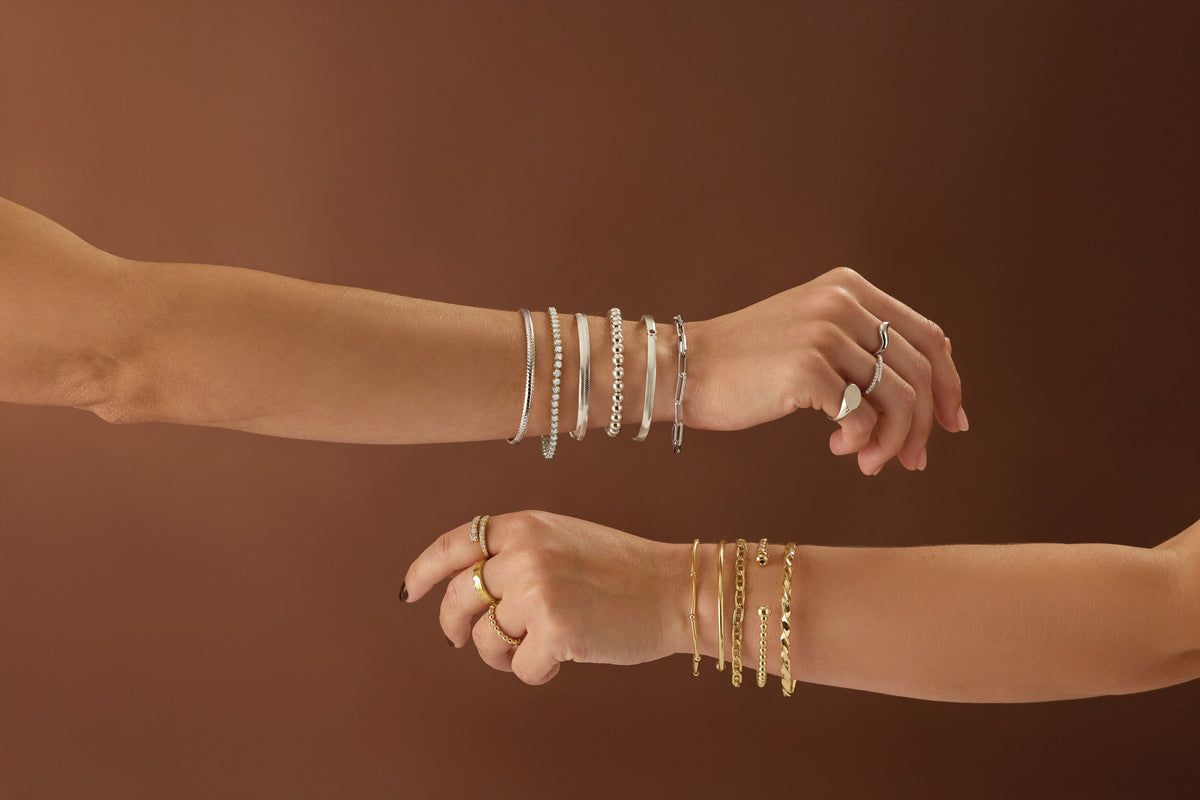 White and yellow gold bracelets stacked on two wrists – Picasso Gold & Diamond Chicago