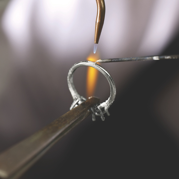 Close-up of a silver ring being heated by a torch with a blurred background