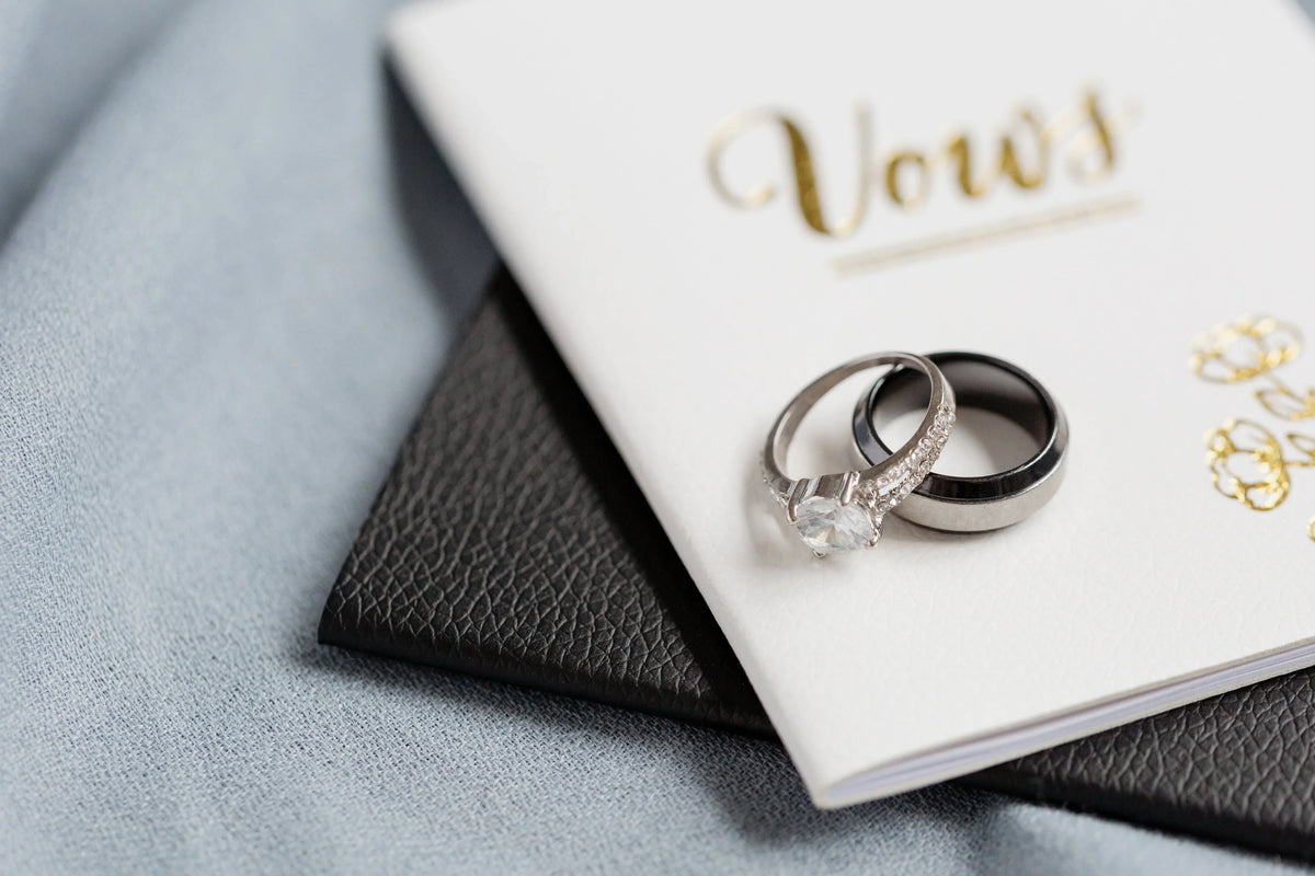 Diamond engagement ring and wedding bands resting on a wedding vows booklet